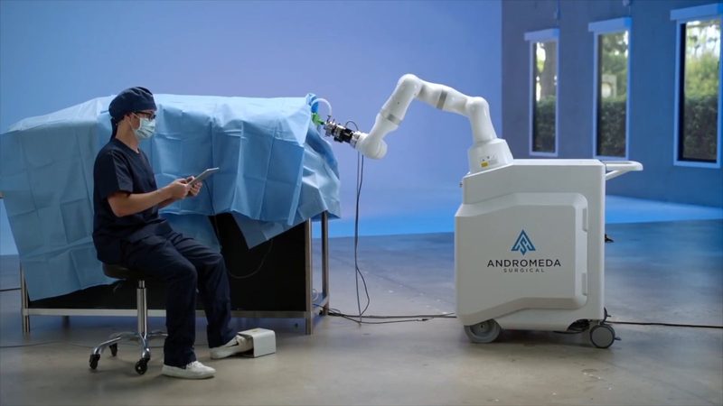 The Andromeda Surgical robot arm positioned at a surgical table with a surgeon seated alongside