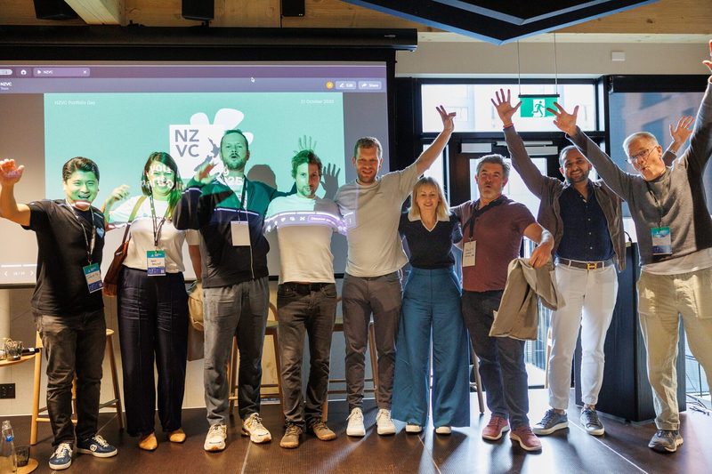 Founders and investors with their arms raised on stage in front of a screen reading NZVC Portfolio Day, 21 October 2025