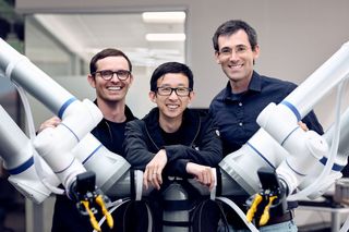 The three Generalist founders behind a pair of robot arms
